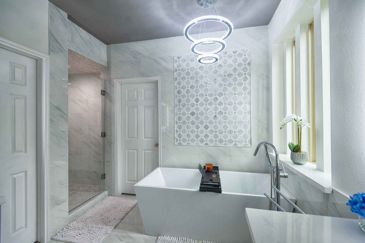 Luxury master bathroom with marble tile walls freestanding soaking tub and LED chandelier in Houston
